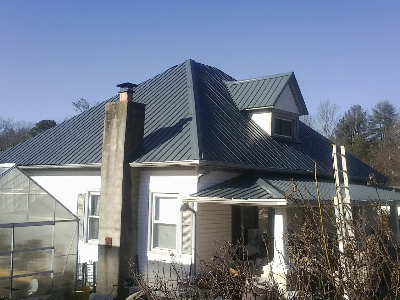 Dark blue standing seam metal roof on a white farmhouse with dormer — Slate & Tile Roof Repair by Roofing Brothers in Granville