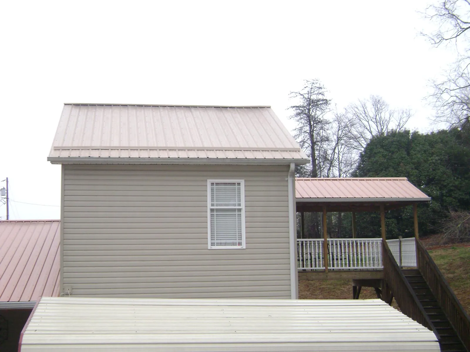 Tan metal roofs on a two story addition and attached porch, from a Roof Replacement job in Granville
